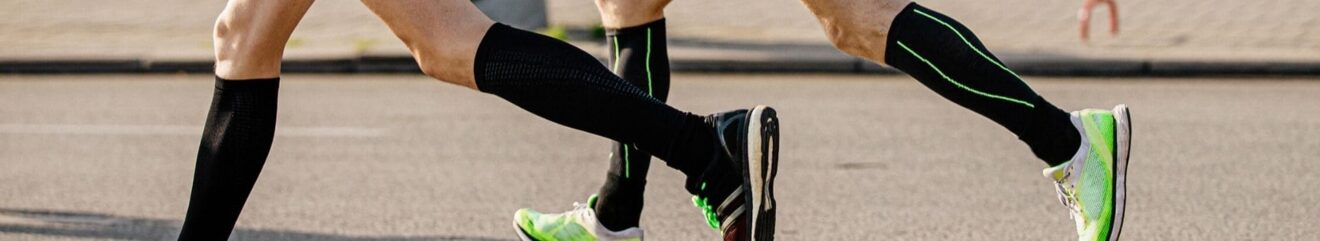 Primo piano delle gambe di due persone che praticano running su asfalto, con calze tecniche e scarpe da corsa verde fluo